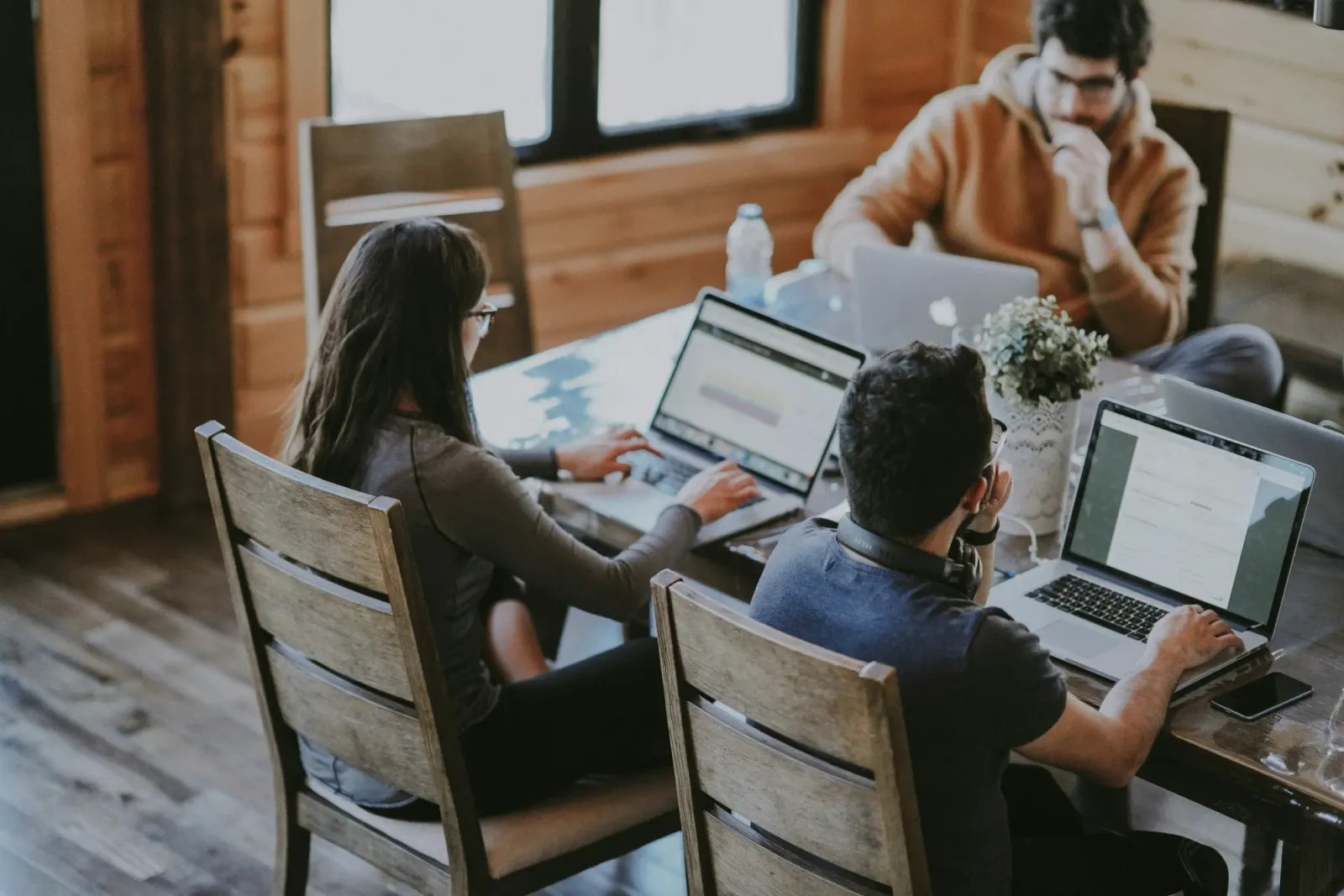 Three people working on laptops around a wooden table, suggesting a small team handling growing service demand.