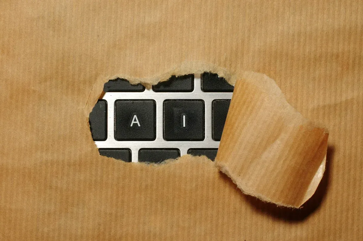 Laptop keyboard keys spelling AI revealed through a tear in brown paper