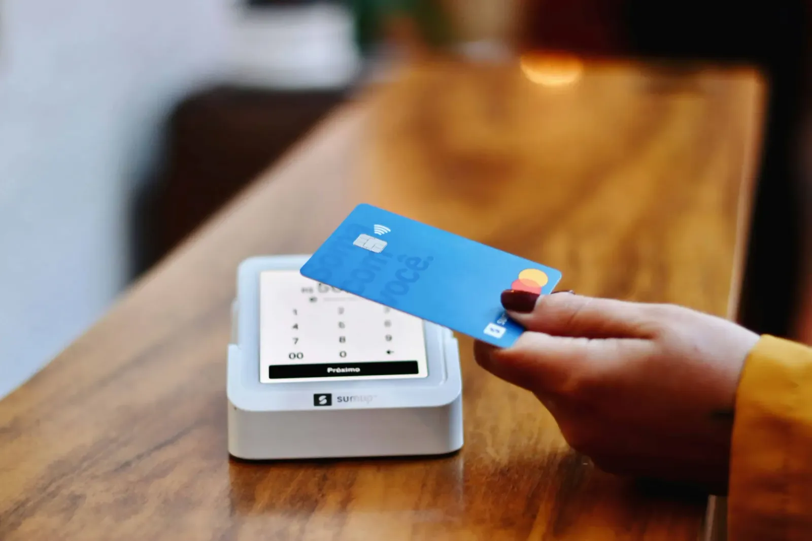 Hand holding a contactless payment card over a card reader on a wooden counter, illustrating prepaid card programs